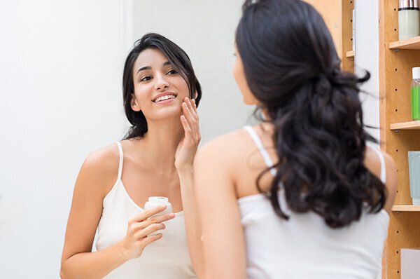 Woman caring of her beautiful skin on the face standing near mirror in the bathroom. Beautiful young